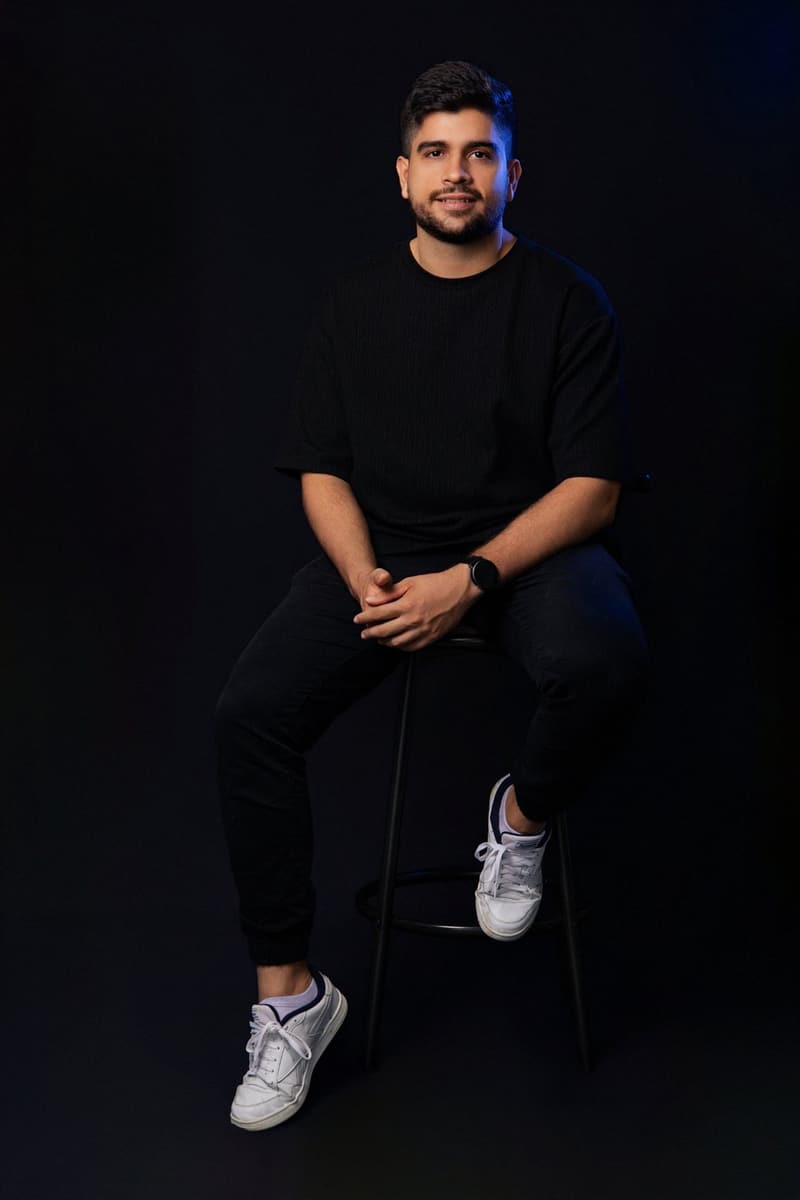 Juan Camilo Rojas sitting on a bench, smiling, black background
